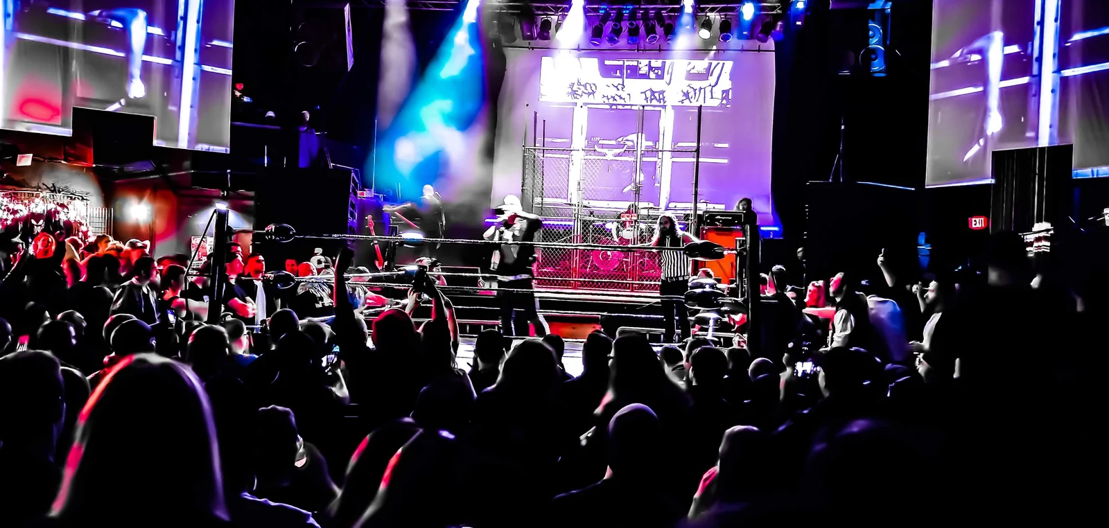 Fans watch a WrestleCore show with dramatic stage lighting behind the ring.