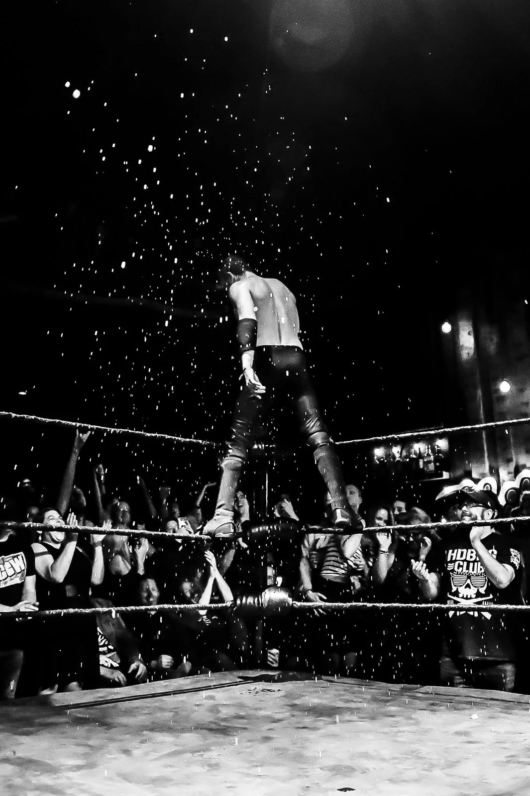 A wrestler stands on the ropes above an enthusiastic WrestleCore crowd.